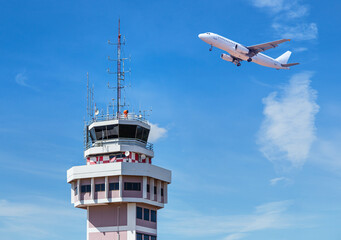 Air traffic control tower in international airport with passenger airplane jet taking off on blue sky background - 570179625