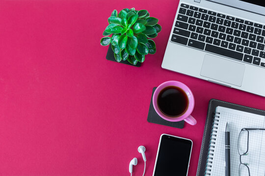 Workplace with laptop, notebook with pen and other items on desktop with burgundy surface. Top view with copy space, flat lay