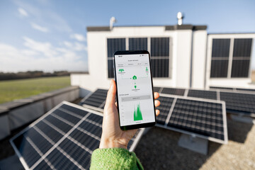 Woman monitors energy production from the solar power plant with mobile phone. Close-up view on phone screen with running program. Concept of remote control of solar energy production - 570185468