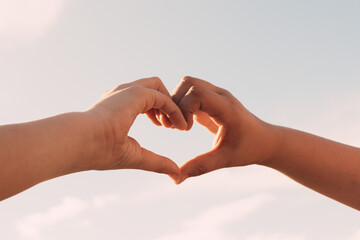 Two sisters joining hands in the shape of a heart in the background of the blue sky, Family