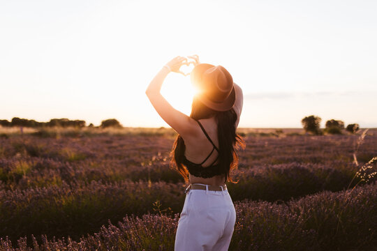 Woman forming a heart with her hands in a lavender field at sunset