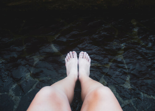 female legs and feet getting wet in the river against river water