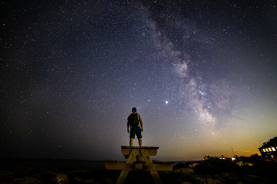 Silhouette of man star gazing on a picnic table under the Milkyway.