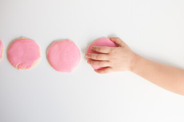 overhead view of child's hand taking pink frosted sugar cookie