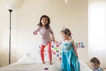 Laughing 6 yr old girl and 4 yr old in princess gown jumping on bed