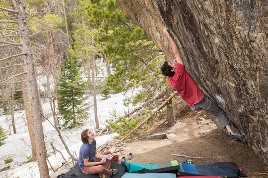 Two men climb outside on a boulder together in the alpine forest