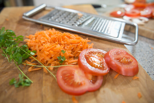 Grated carrots with sliced tomatoes, parsley and grater in background, close up