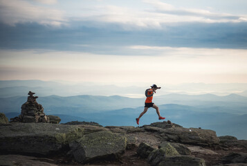 Trail runner man running along ridge with cairn and mountains