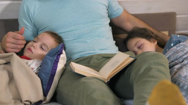 Caring father reading bedtime story to his children at home. Evening family reading. Kids listening dad, reading a fairytaleA fairytale before going to bed. People and family concept. Happy childhood
