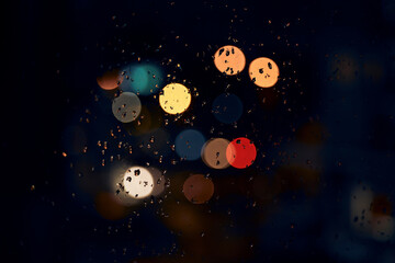 Night, bokeh and lights on a window with water drops, liquid or moisture against a dark abstract background. Blurred light, colorful and rain drop or splash on glass for city view during rainy season