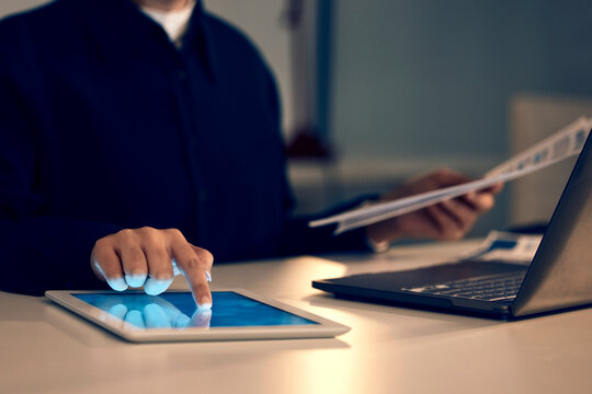 Hand, tablet and laptop in night at office for research, analysis and web design at desk for tech innovation. Man, mobile touchscreen and iot with documents for goal, search and coding on website ui