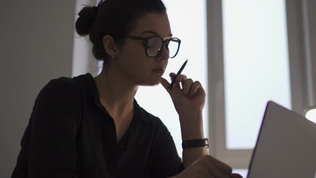Serious woman analyst checking data on laptop and making notes to notepad