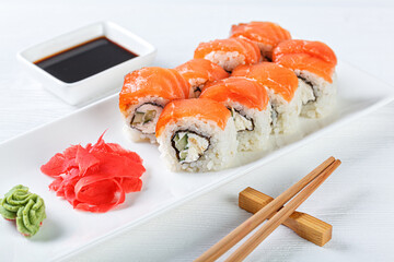 Sushi with salmon on a white plate with wasabi, ginger, soy, chopsticks on a white background