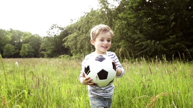 Little boy running through tall grass with soccer ball