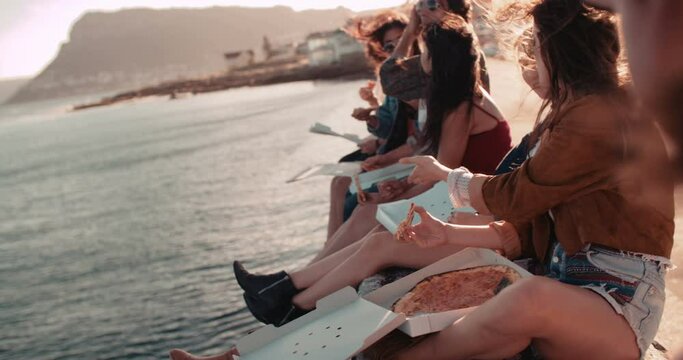 Group of hipster friends eating pizza sitting on the dock at the harbor during a summertime road trip