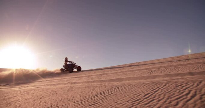 Professional quad biker racing downhill over a sand dune in a desert race in Slow Motion