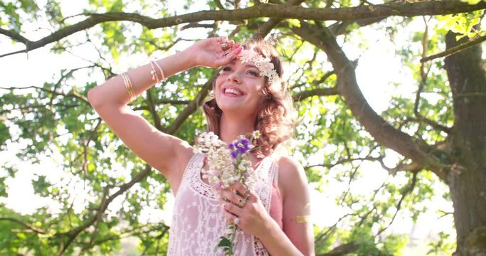 Teenaged girl in boho style clothing laughing happily with her eyes closed and holding a spray of wild flowers in a sunny summer park