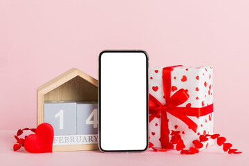 mobile phone with blank screen on colored background with hearts, calendar and gift box, valentine day 14 february concept perspertive view flat lay