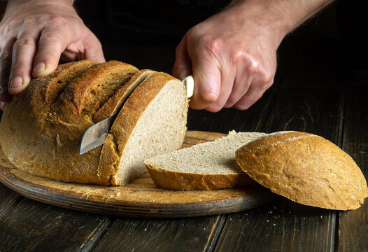 The chef hands with a knife slices bread on a kitchen cutting board. The concept of healthy food in the bakery. Copy space