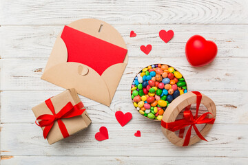 Red envelope with candy and gift box and Valentines hearts on colored background. Flat lay, top view. Romantic love letter for Holiday concept