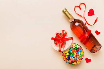 Bottle of red wine on colored background for Valentine Day with gift and chocolate. Heart shaped with gift box of chocolates top view with copy space