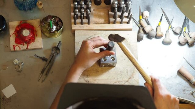 Handheld cropped image of female artist hammering dapping punches on doming block at workbench in workshop