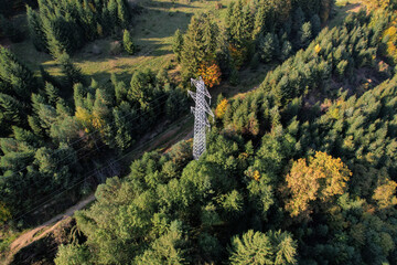 Aerial view of a high voltage suspension tower on a hillside, surrounded by trees. The autumn sun...