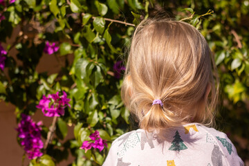 Naklejka premium Little girl with backpack standing in front of green with violet flowers