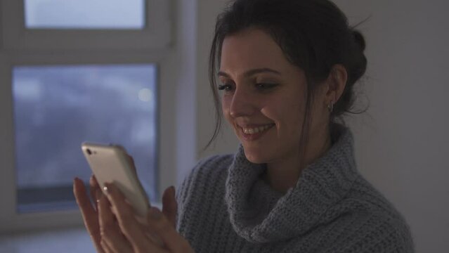 Young woman scrolling through news feed in social networks on smartphone and smiling, reading news, commenting and rating posts