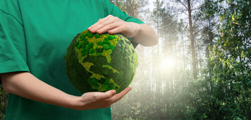 Woman  holds a green planet Earth on a background of forest. Symbol of sustainable development and renewable energy