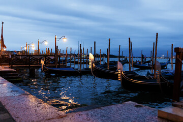 evening and rows of gondolas stand near the pier in Venice