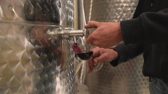 A man pours himself red wine in a glass, straight from the stainless