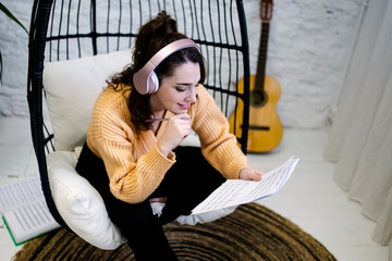 Young Woman with headphones and a guitar composing music at home