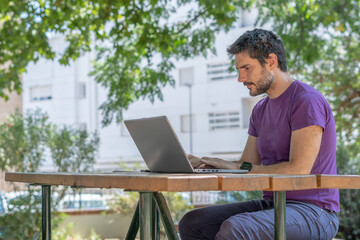 young man with beard in profile working with his pc in the park