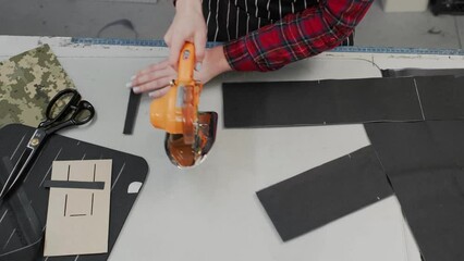 Seamstress at work. Dressmaker cutting fabric with professional machine. Woman standing at table with cut textile and working on a design. Top view, closeup with copy space. Disc cutting knife