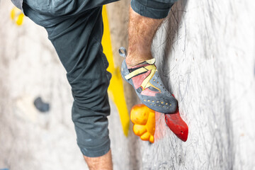 Close up view of young man or climber feet in climbing shoes on artificial indoor wall at climbing...