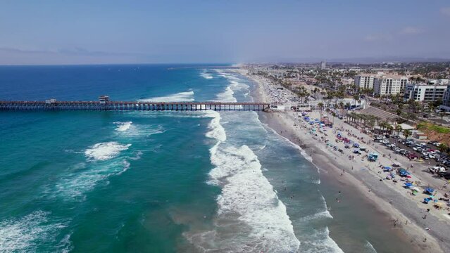 Drone Flying Over Oceanside Beach Towards Pier and Beachfront Resorts