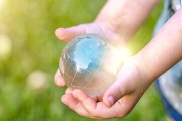 Glass globe in girl hand on blurred green grass banner background with sunlight in city. Concept of environment world earth day. Protect clean nature and ecology, sustainable lifestyle, save planet