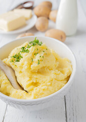 Homemade mashed potatoes in a white bowl with wooden spoon and ingredients in the background