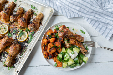 Baked chicken drumsticks with sweet potatoes and cucumber salad on a plate 