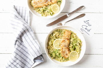 Low carb dinner or lunch with pan fried fish fillet and creamy zucchini noodles . Served on plates on white background with cutlery