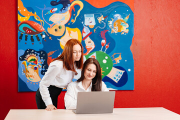 Obraz premium two women work together in an office on a laptop. 