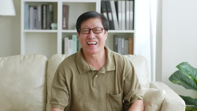 Portrait happy Asian senior man look at camera then smile and laugh at home