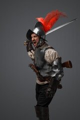 Studio shot of isolated on gray background soldier with epee dressed in plate armor.