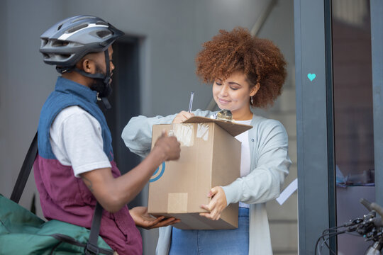 Black Man, Box And Customer Signing In Ecommerce For Delivery Service, Package Or Order At Door. Happy African American Female With Courier Guy With Signature On Clipboard For Quality Or Feedback