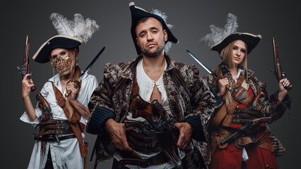 Studio shot of crew of corsair man and two female pirates looking at camera.
