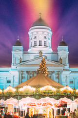 Fototapeta premium Helsinki, Finland. Xmas Market On Senate Square With Holiday Carousel And Famous Landmark Is Lutheran Cathedral At Winter Evening. Amazing Sky Clouds. Very Peri. Bright Purple Lavander Colors Of Sky.
