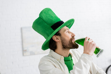 Side view of man in hat drinking green beer during saint patrick celebration at home