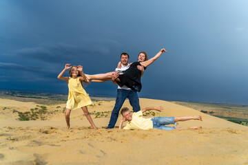 Happy family of mother, father, daughter and son jumping, laughing and having fun in sand dunes on vacations. Happy family of four jumping on high sand dune at mountains