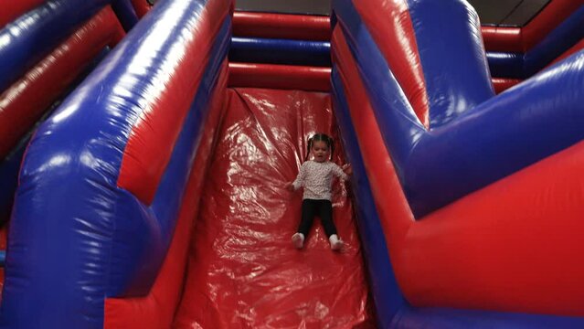 4K:  Little girl sliding down a red Inflatable Slide in a play area. Indoors.  Stock video clip footage